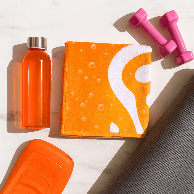 An orange gym towel with a water droplet design, along with a drink bottle and pink dumbbells on a grey mat.