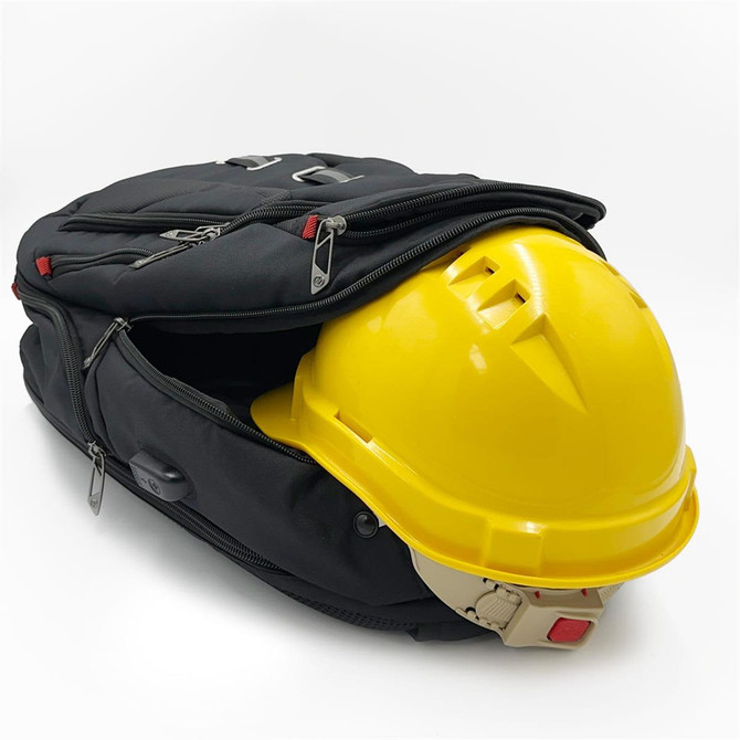 A black backpack partially unzipped, revealing a yellow hard hat inside. The backpack features zippers and a logo.