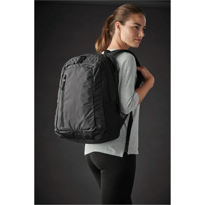 A black laptop bag is worn on one shoulder by a woman, showing its practical design and padded straps.
