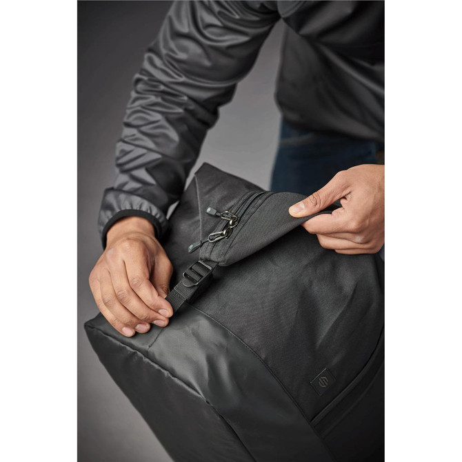 A person holding a black duffle bag, partially unzipping it, showcasing its sleek design and a logo.