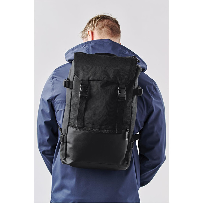 A black backpack with adjustable straps is worn on the back of a person, who is facing away from the camera.