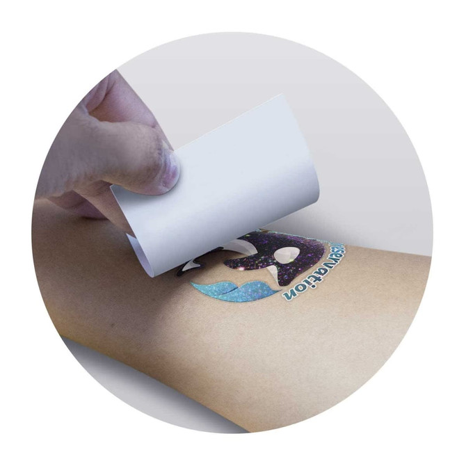A hand applying a colourful temporary tattoo featuring a galaxy design on a light skin tone.