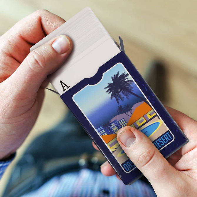 A person holding a blue box of Vegas Playing Cards with a palm tree design, revealing an Ace card.
