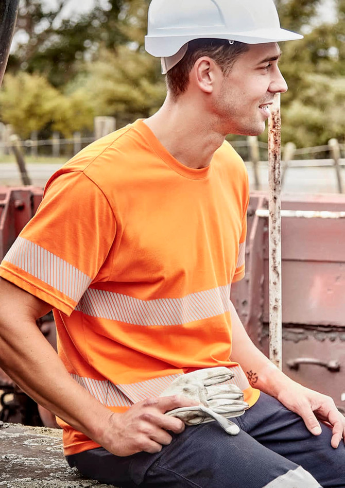 An orange hi-visibility cotton tee with segmented reflective tape, worn by a man in a hard hat, sitting outdoors.