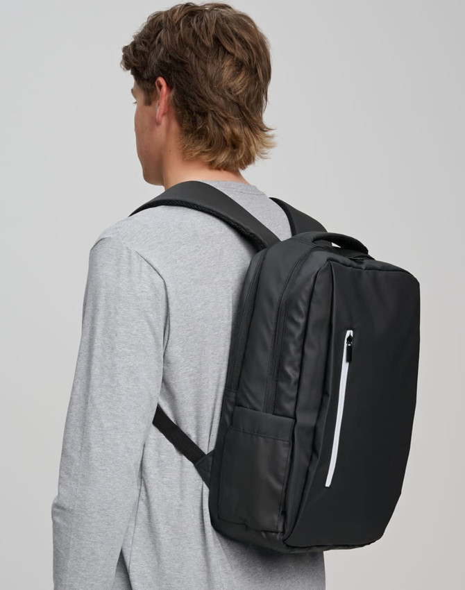 A black backpack with multiple compartments is worn on the back of a person in a grey top. The backpack features a logo.