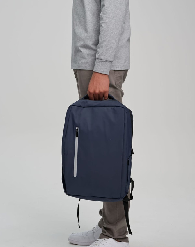 A navy blue PU backpack is being held by a person. The backpack features a zipper and has a logo.