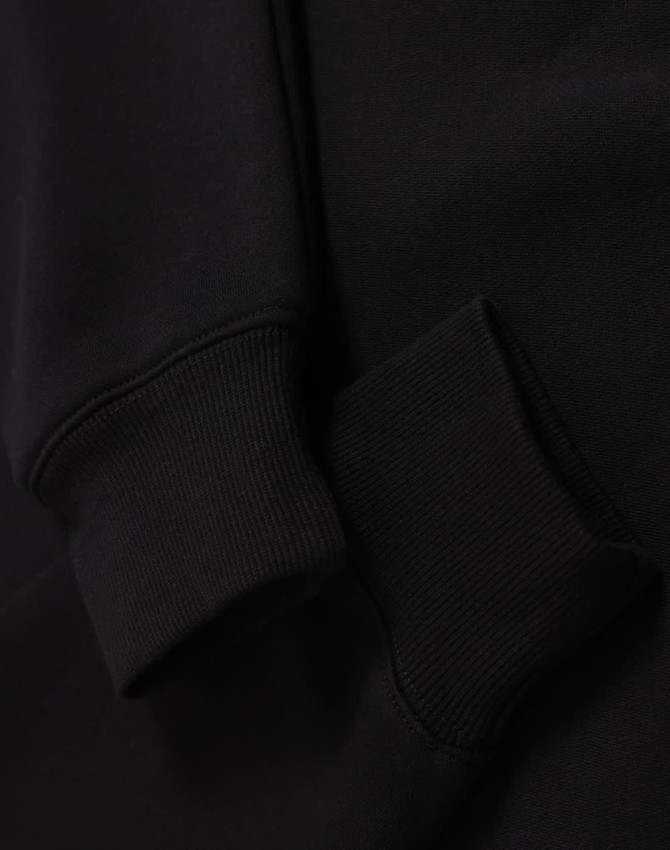 A black unisex premium fleece oversized hoodie with ribbed cuffs. The fabric appears soft and cozy.