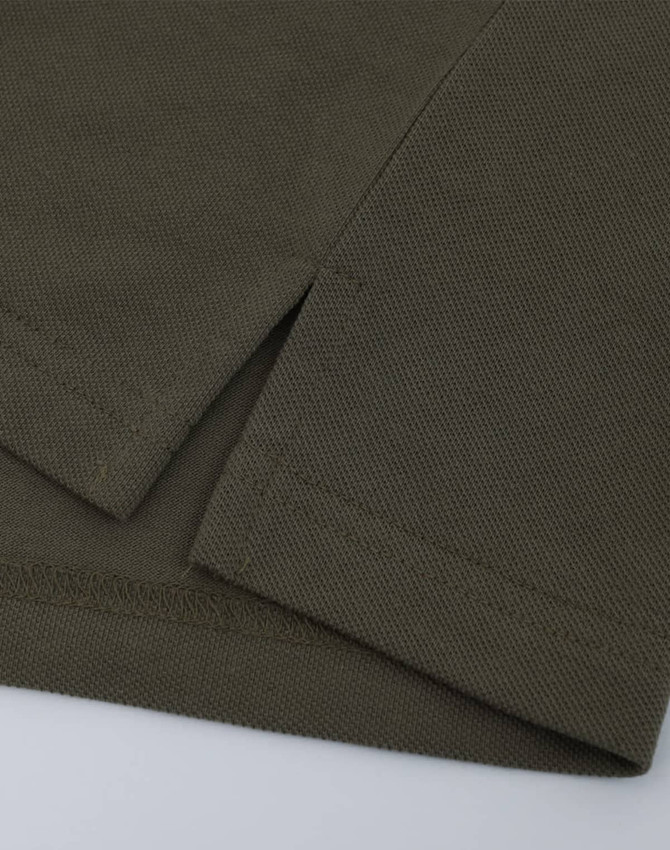 A close-up of a short-sleeved polo in an olive green cotton/poly pique fabric with a stitched hem.