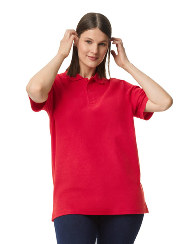 A woman wears a red Gildan Hammer adult double pique polo shirt, styled with a relaxed fit. The shirt features a logo.