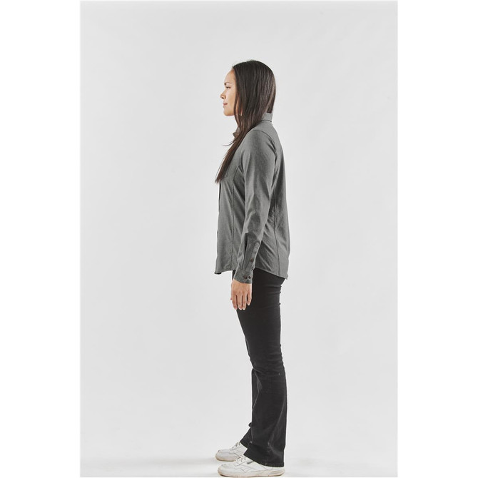 A side view of a woman wearing a grey button-up shirt and black pants, standing with a neutral expression.