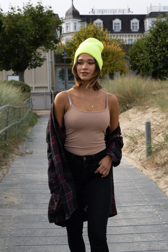 A beanie in bright yellow worn by a model with a casual outfit, walking along a beachside path.