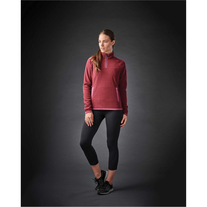 A woman wearing a burgundy women's fleece jumper with a 1/4 zip and black leggings, featuring a branding logo.