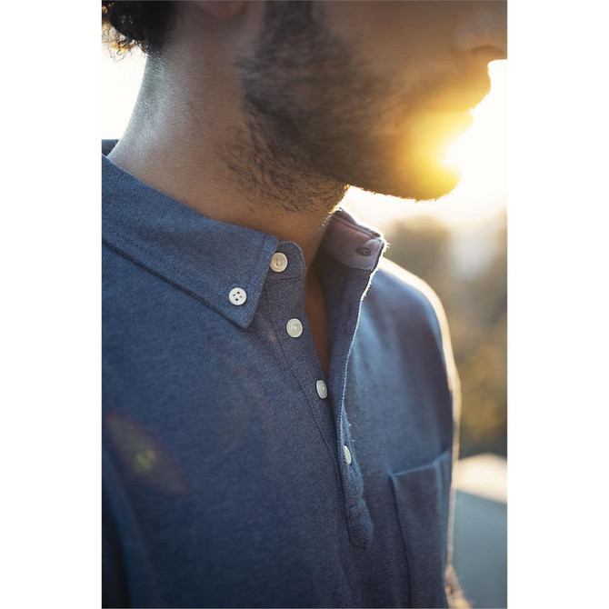 A men's polo shirt in blue with a collar, buttons, and a chest pocket, featuring soft lighting effects.