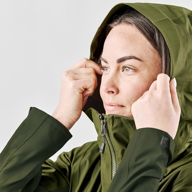 A woman adjusts the hood of a green jacket. The jacket features a logo and has a sleek design.