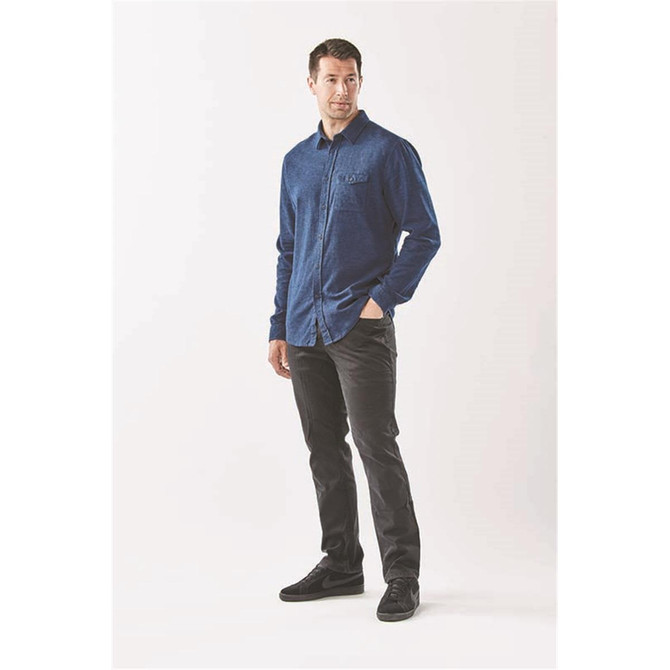 A man wears a navy long sleeve twill button-up shirt paired with black pants and shoes. The shirt has a logo.