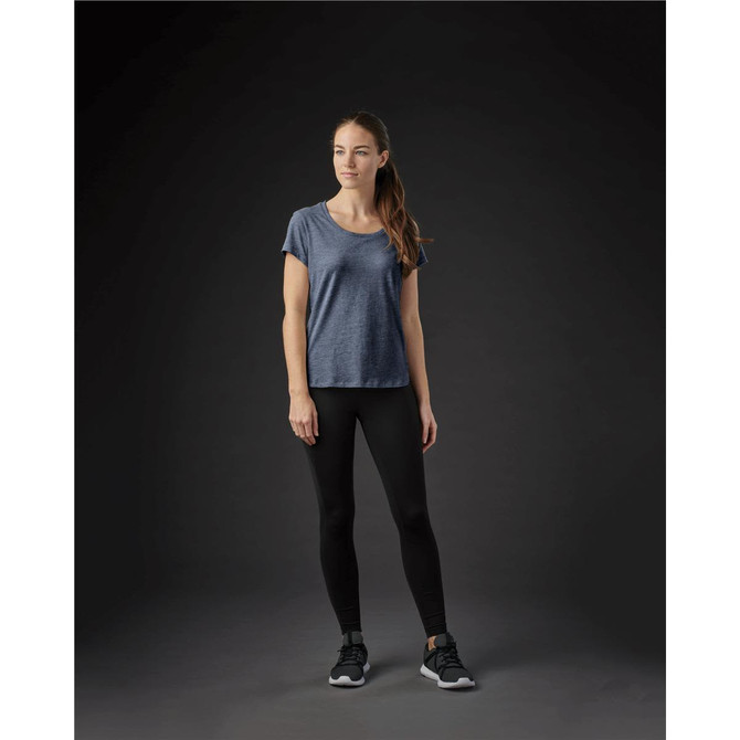 A woman stands in a navy blue crew neck t-shirt and black leggings, with a subtle logo on the shirt.