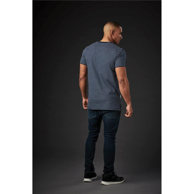 A man wearing a navy and white striped crew neck tee, paired with dark jeans, viewed from the back against a dark background.
