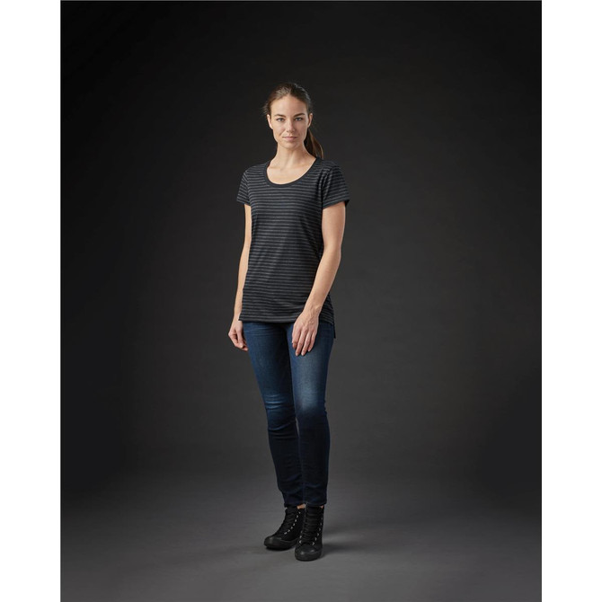 A woman stands in a fitted black and grey striped crew neck t-shirt, paired with dark jeans and ankle boots.