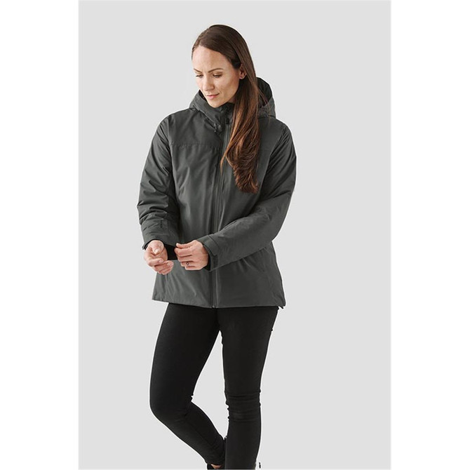 A woman wearing a dark green thermal shell jacket with a hood, featuring a logo on the jacket.