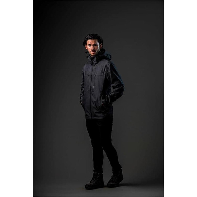 A model wearing a black Men's Patrol Softshell jacket, standing against a dark background. The jacket features a hood and has branding.