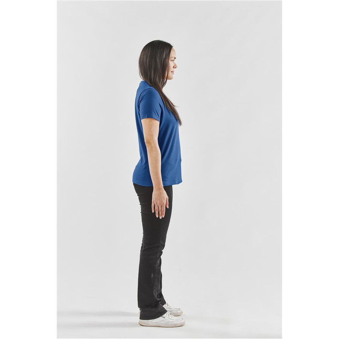 A woman stands sideways wearing a blue Settebello T-shirt and black pants, with a logo visible on the shirt.