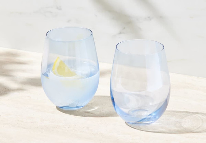 A set of two stemless wine glasses in pale blue, one filled with water and a slice of lemon.
