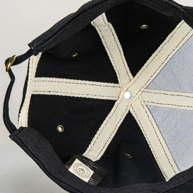 An organic cap featuring a black exterior with a light-coloured lining and internal stitching details.