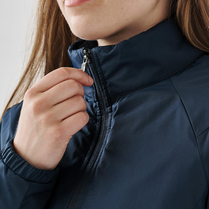 A close-up of a woman's hand adjusting the zipper of a navy thermal jacket with a high collar.