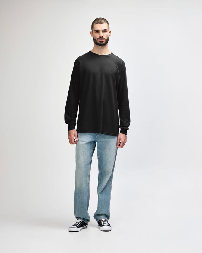 A long sleeve t-shirt in dark grey worn by a model, paired with black trousers and sneakers.