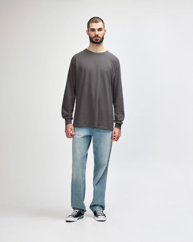 A long-sleeve T-shirt in grey worn by a model, paired with black jeans and sneakers. The shirt features a logo.