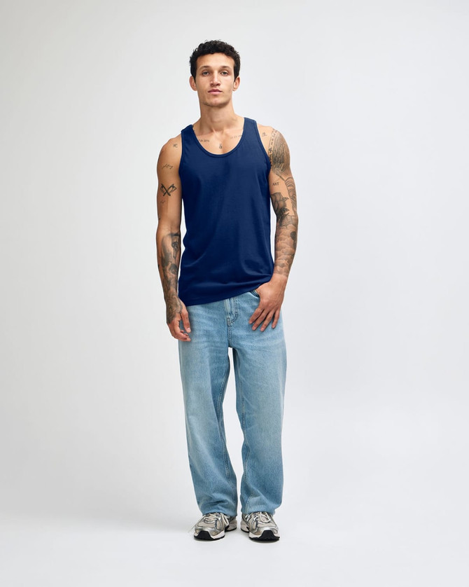 A model wearing a navy blue unisex fine jersey tank top paired with black cargo pants and sneakers.