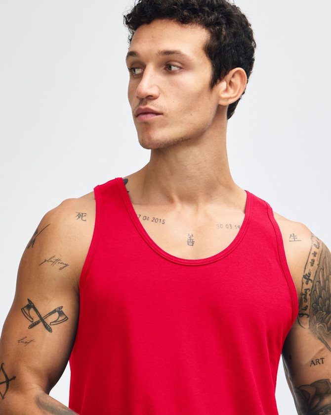 A red unisex fine jersey tank top with a relaxed fit and logo. Model is adjusting the straps.