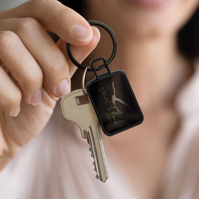 A key ring featuring a rectangular design in black, attached to a metal key, held by a person.