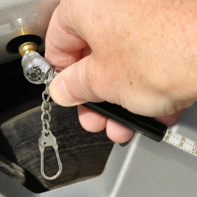 A tyre pressure gauge key ring with a silver and black design, being used to check tyre pressure.