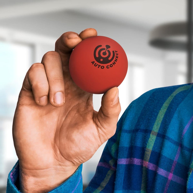 A hand holds a red Hi-Bounce Ball featuring a logo, set against a blurred indoor background.