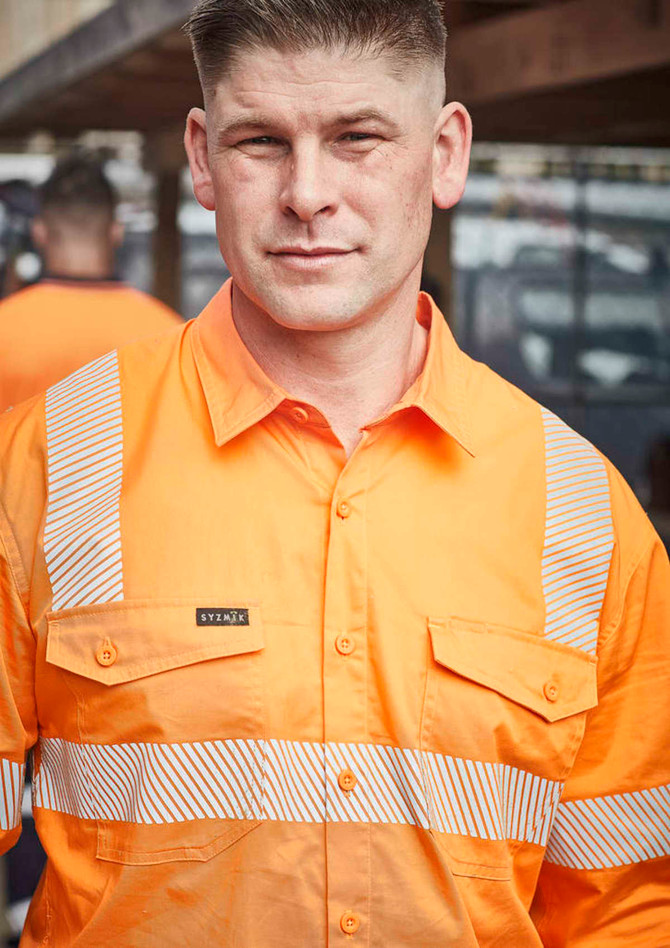 A man wearing an orange work shirt with segmented reflective tape and a logo on the front.