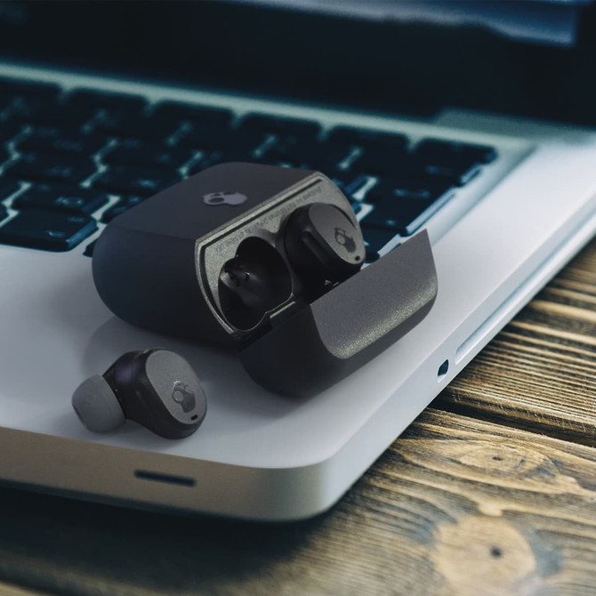 A pair of black Skullcandy Mod TWS earbuds and their charging case on a laptop keyboard.