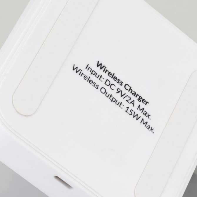 A wireless charging stand in white with a smooth surface and a branding logo on the base.