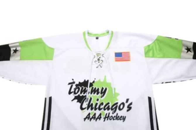 A white ice hockey jersey with green sleeves and a logo, featuring an American flag patch on the front.