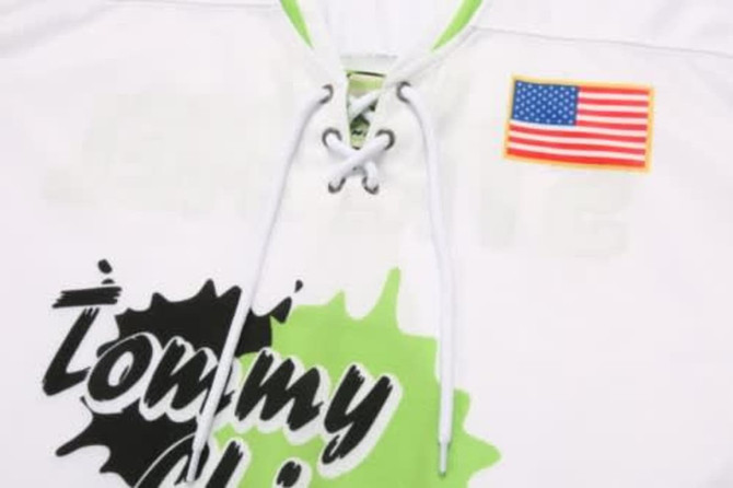 A white ice hockey racing suit featuring green accents and a logo, with an American flag on display.