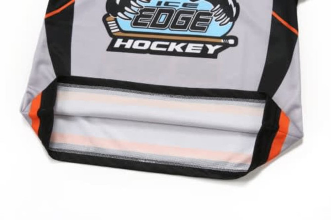 A grey ice hockey jersey featuring orange accents and a logo at the front, with a stitched hem and black details.