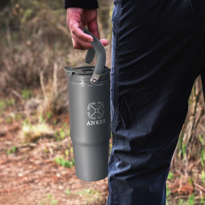 A drink bottle with a grey finish and a handle, featuring a brand logo, held by a person outdoors.