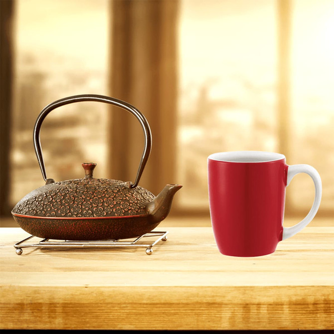A red ceramic mug next to a decorative teapot on a wooden surface, set against a blurred background.