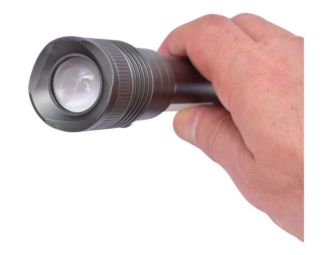 A gunmetal torch with a textured grip held in a person's hand, featuring a round lens at the front.
