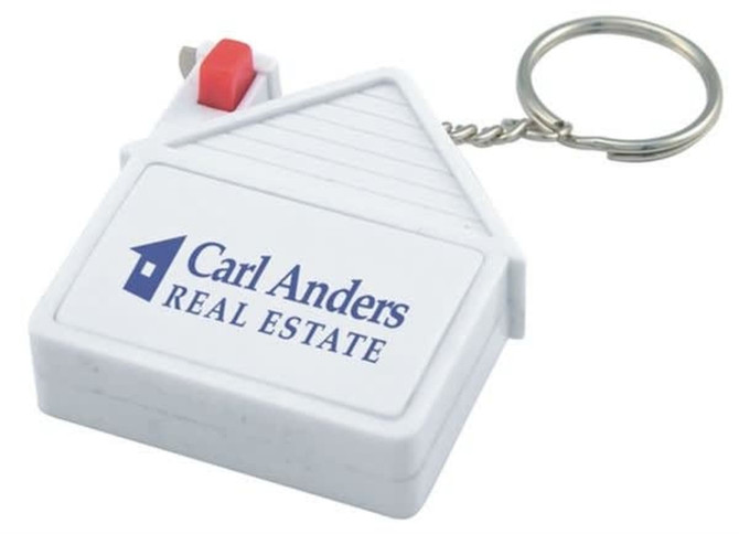 A house-shaped tape measure in white with a keyring attachment and a red button, featuring a logo.