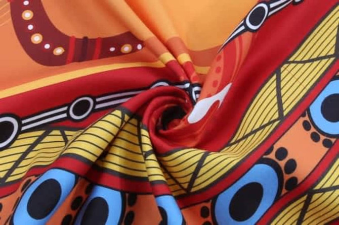 A vibrant beach towel featuring a bold pattern with orange, red, yellow, and blue colours. It has a logo.