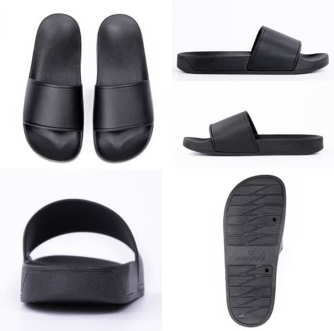 Black slippers featuring a simple design with a flat sole and a wide strap. Contains a logo on the side.