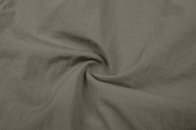 A fabric swatch of light beige windbreaker pants, featuring a smooth texture and a subtle spiral fold.
