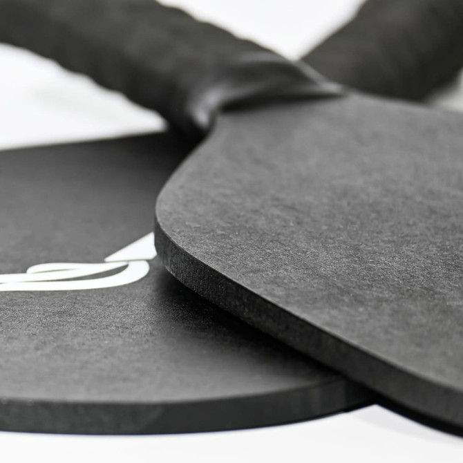 A black pickleball paddle and ball set with a textured grip, featuring a logo on one item.