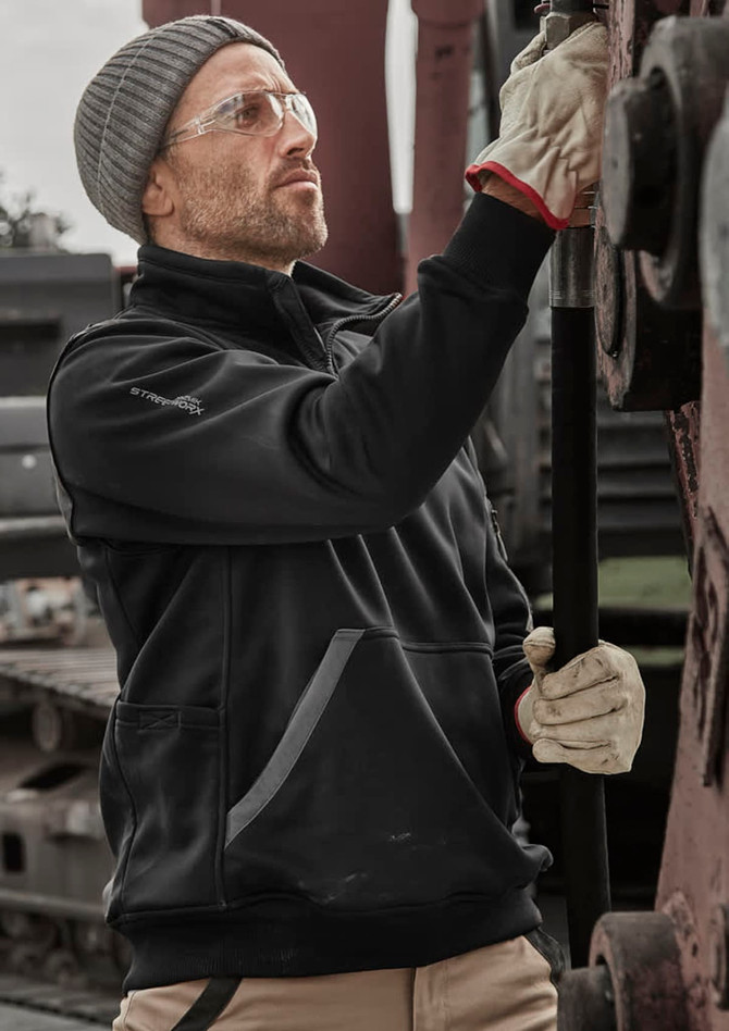 A black water-resistant 1/4 zip pullover worn by a person with safety glasses and gloves, working with machinery.